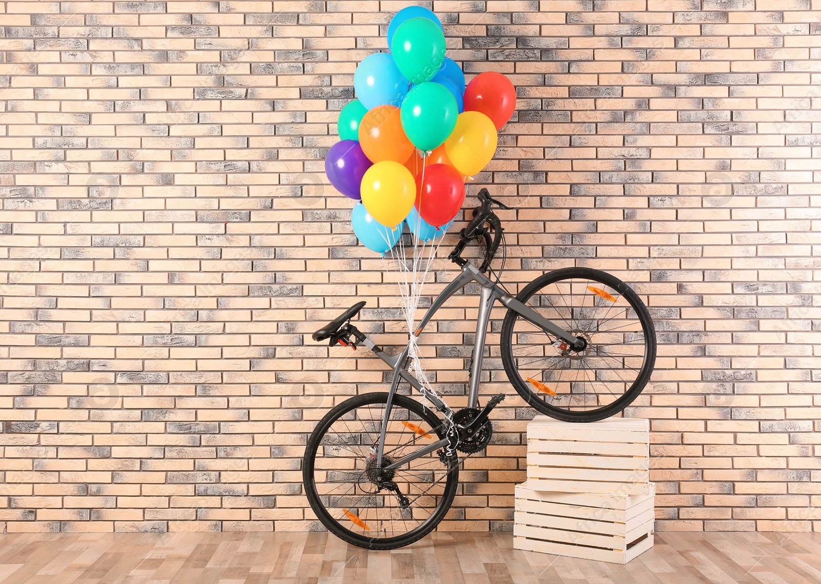 Photo of Bicycle with colorful balloons near brick wall indoors