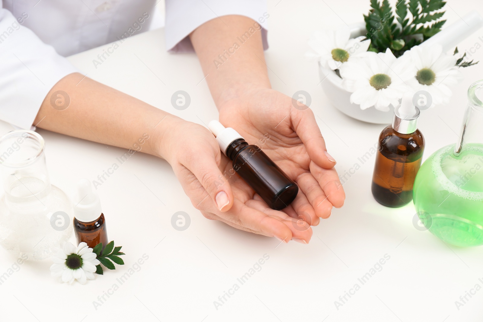 Photo of Female dermatologist holding bottle of skin care product at table, closeup