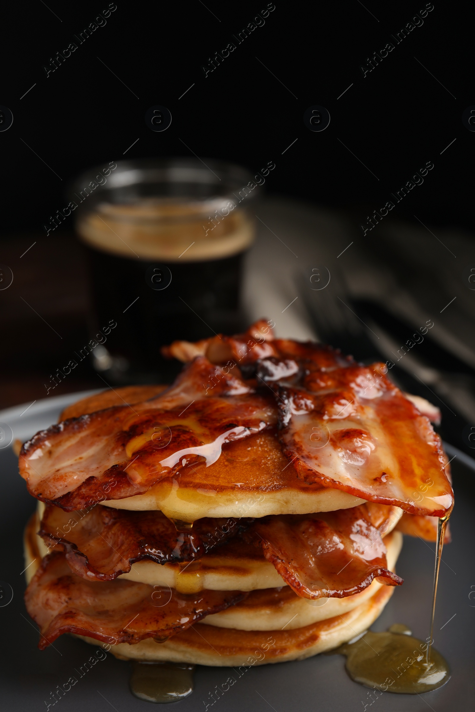 Photo of Delicious pancakes with maple syrup and fried bacon on plate, closeup