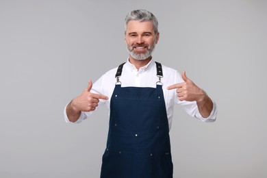 Photo of Happy man pointing at kitchen apron on grey background. Mockup for design