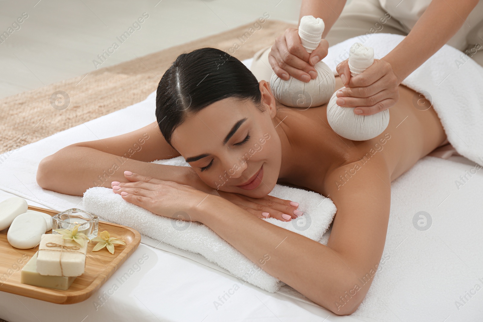 Photo of Young woman receiving herbal bag massage in spa salon