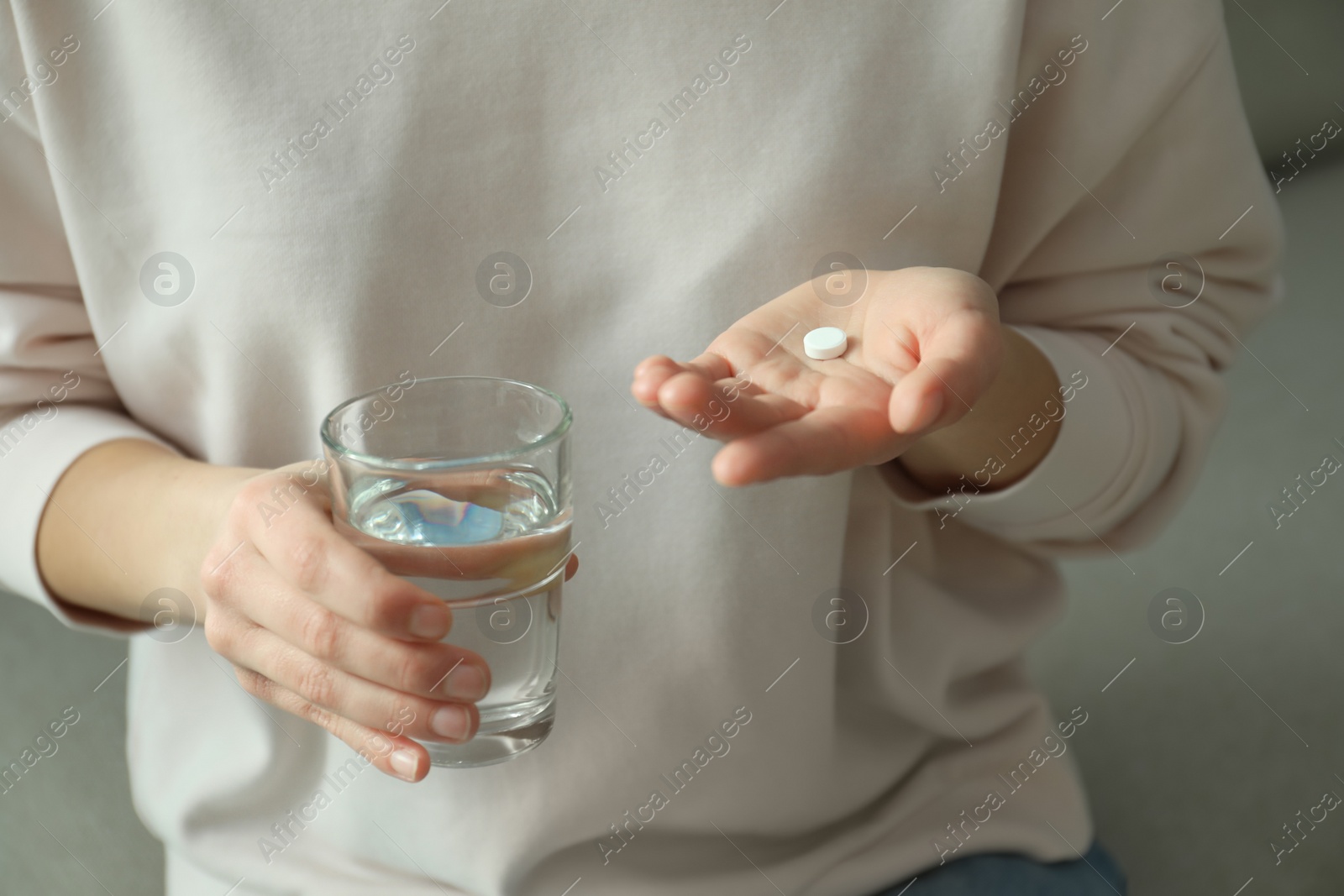 Photo of Young woman with abortion pill and glass of water on sofa, closeup