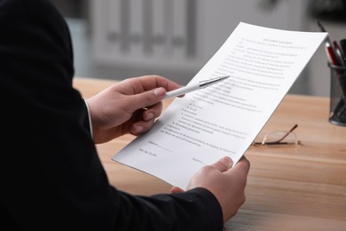 Man reading employment agreement at table in office, closeup. Signing contract