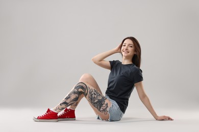 Smiling tattooed woman posing on grey background