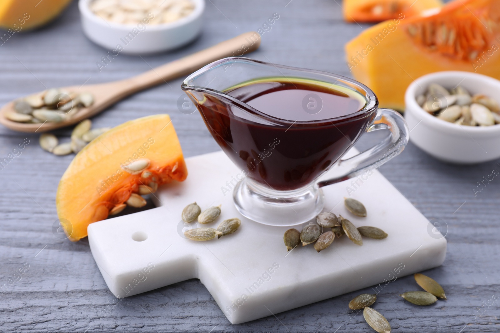 Photo of Fresh pumpkin seed oil in glass sauceboat on grey wooden table