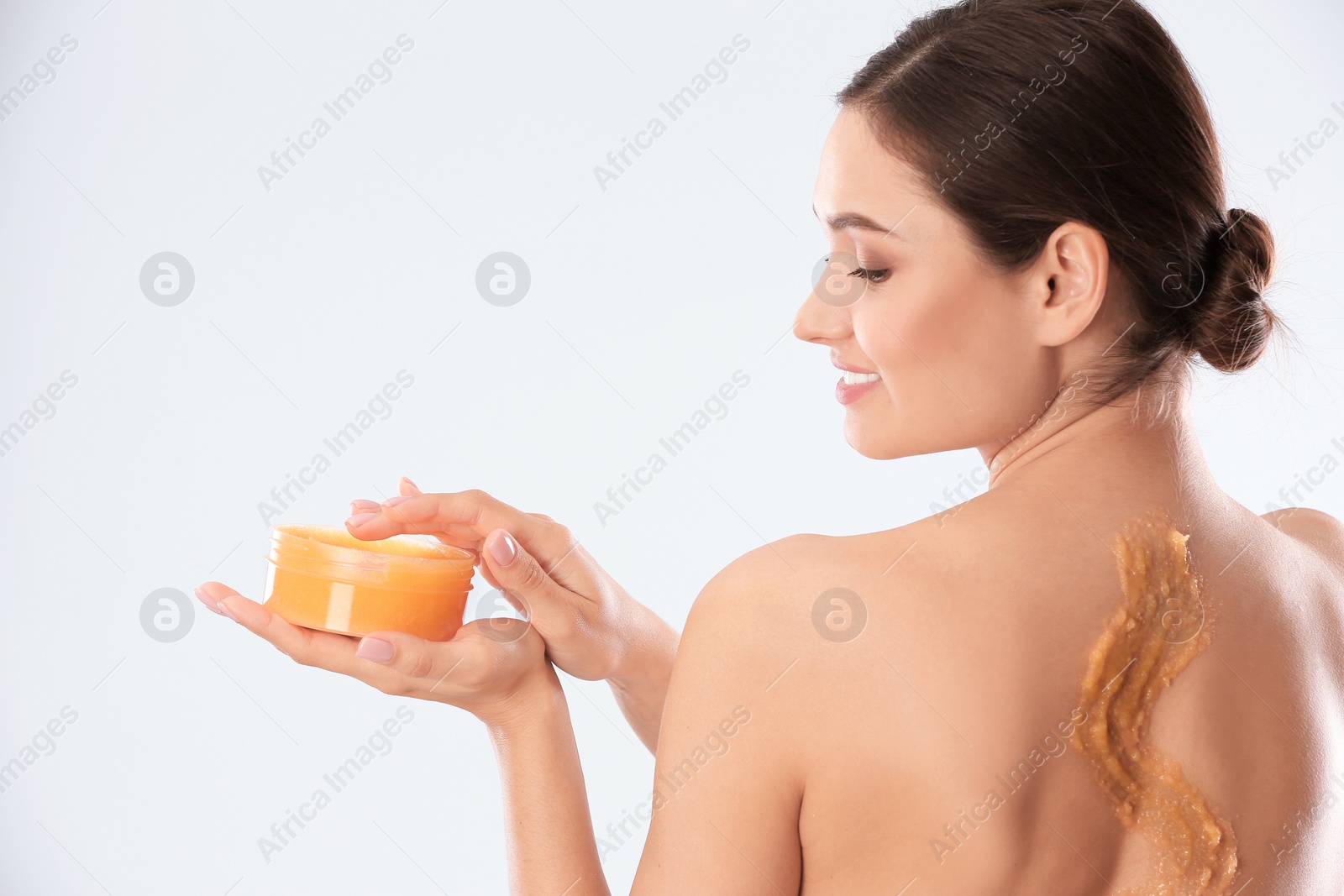 Photo of Young woman applying natural scrub on her body against light background