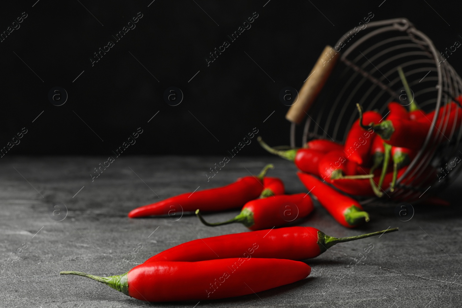 Photo of Red hot chili peppers and metal basket on grey table. Space for text
