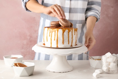 Photo of Young woman decorating delicious caramel cake at table