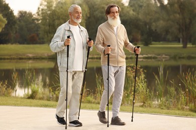Photo of Two senior friends performing Nordic walking outdoors