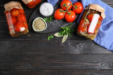 Photo of Flat lay composition with pickled tomatoes in glass jars on black wooden table, space for text