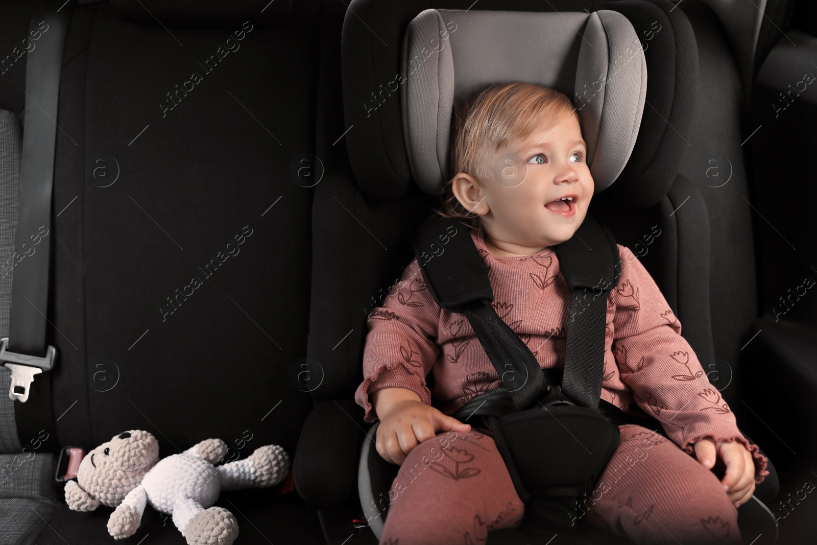 Photo of Cute little girl sitting in child safety seat inside car