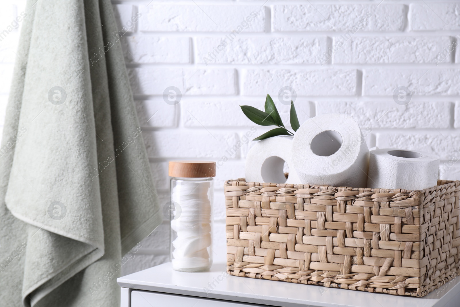 Photo of Toilet paper rolls in wicker basket, floral decor and cotton pads on chest of drawers