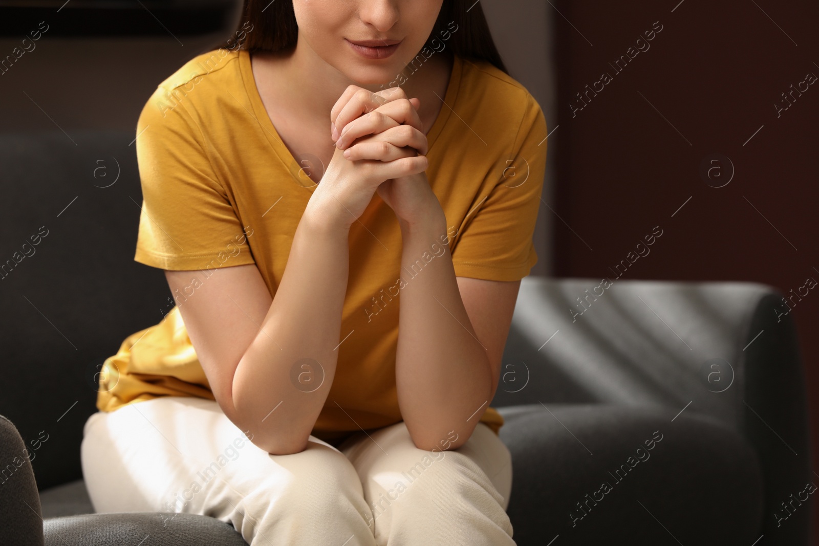 Photo of Religious woman with clasped hands praying indoors, closeup