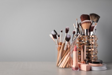 Set of professional brushes and makeup products on table against grey background, space for text