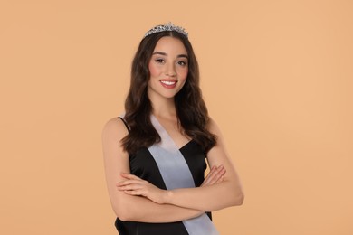 Photo of Beautiful young woman with tiara and ribbon in dress on beige background. Beauty contest