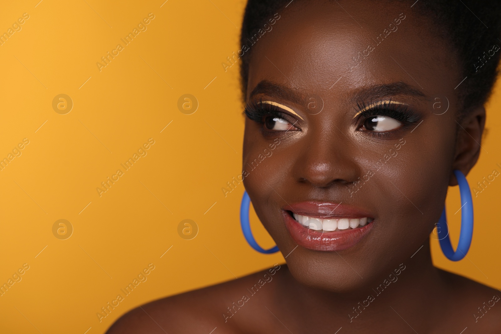 Photo of Fashionable portrait of beautiful happy woman with makeup on orange background, closeup. Space for text