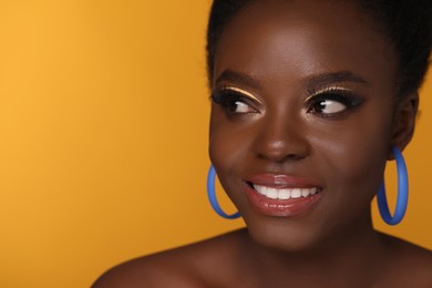 Photo of Fashionable portrait of beautiful happy woman with makeup on orange background, closeup. Space for text
