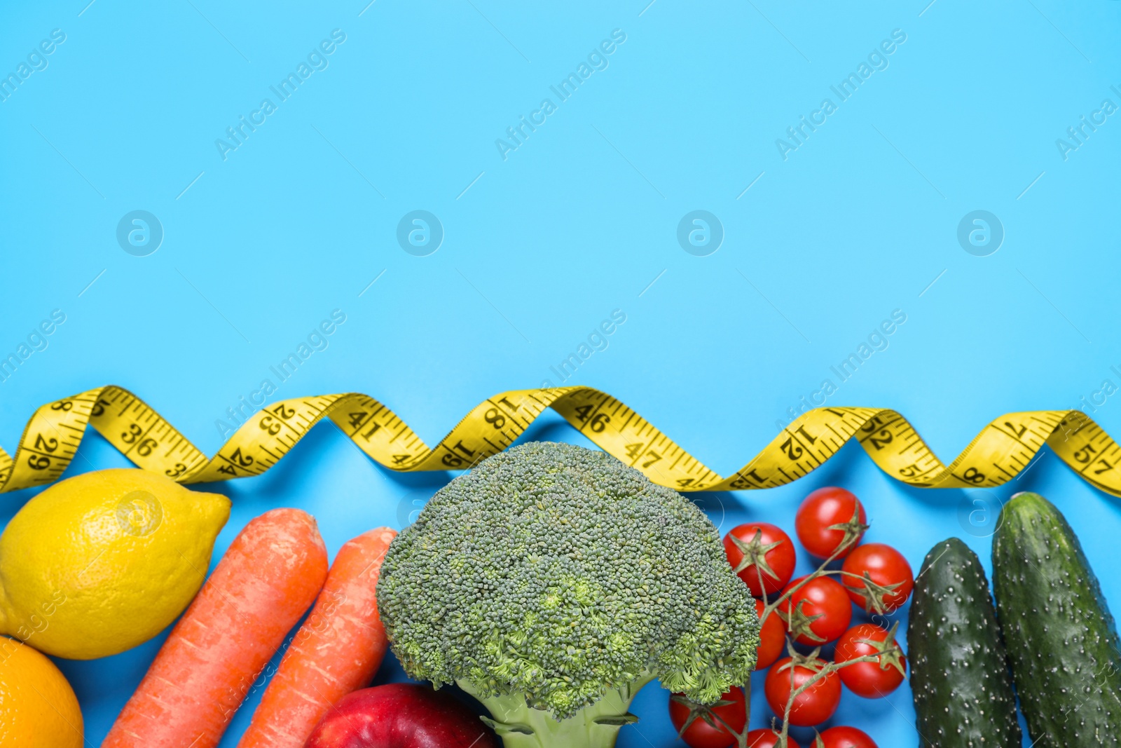 Photo of Measuring tape, fresh lemon and vegetables on light blue background, flat lay with space for text. Low glycemic index diet