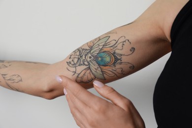 Photo of Woman applying cream on her arm with tattoos against light background, closeup