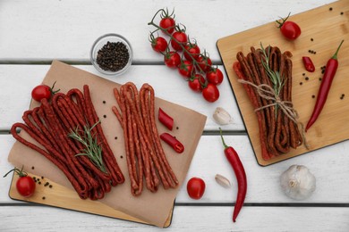 Delicious kabanosy with rosemary, peppercorn, chilli and tomatoes on white wooden table, flat lay
