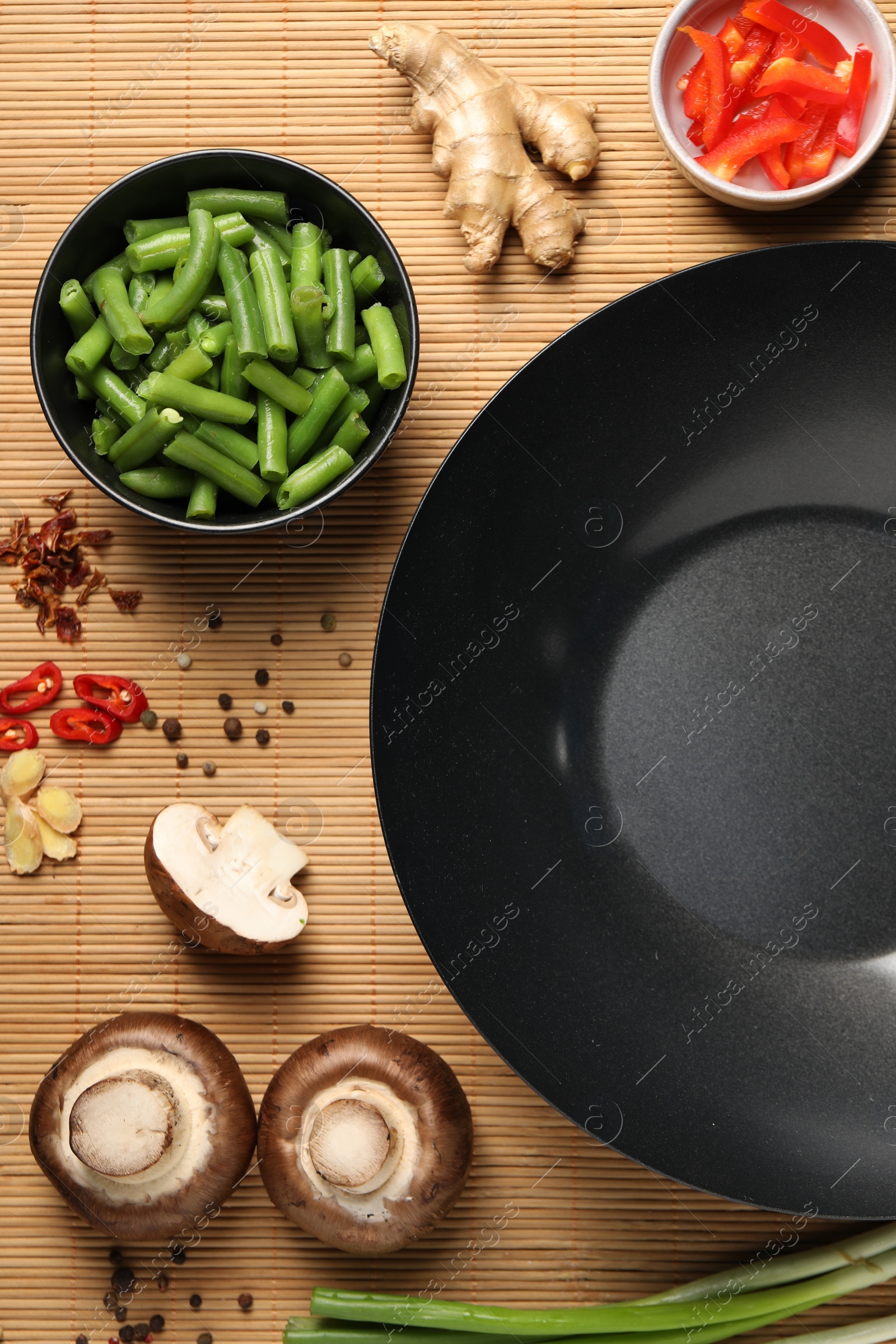 Photo of Flat lay composition with black wok, spices and products on bamboo mat