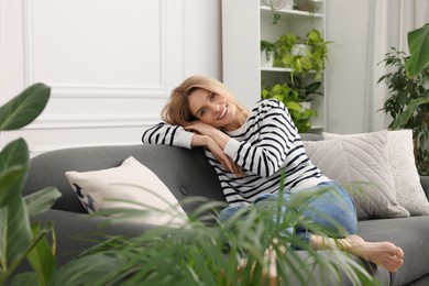 Woman relaxing on sofa surrounded by beautiful potted houseplants at home