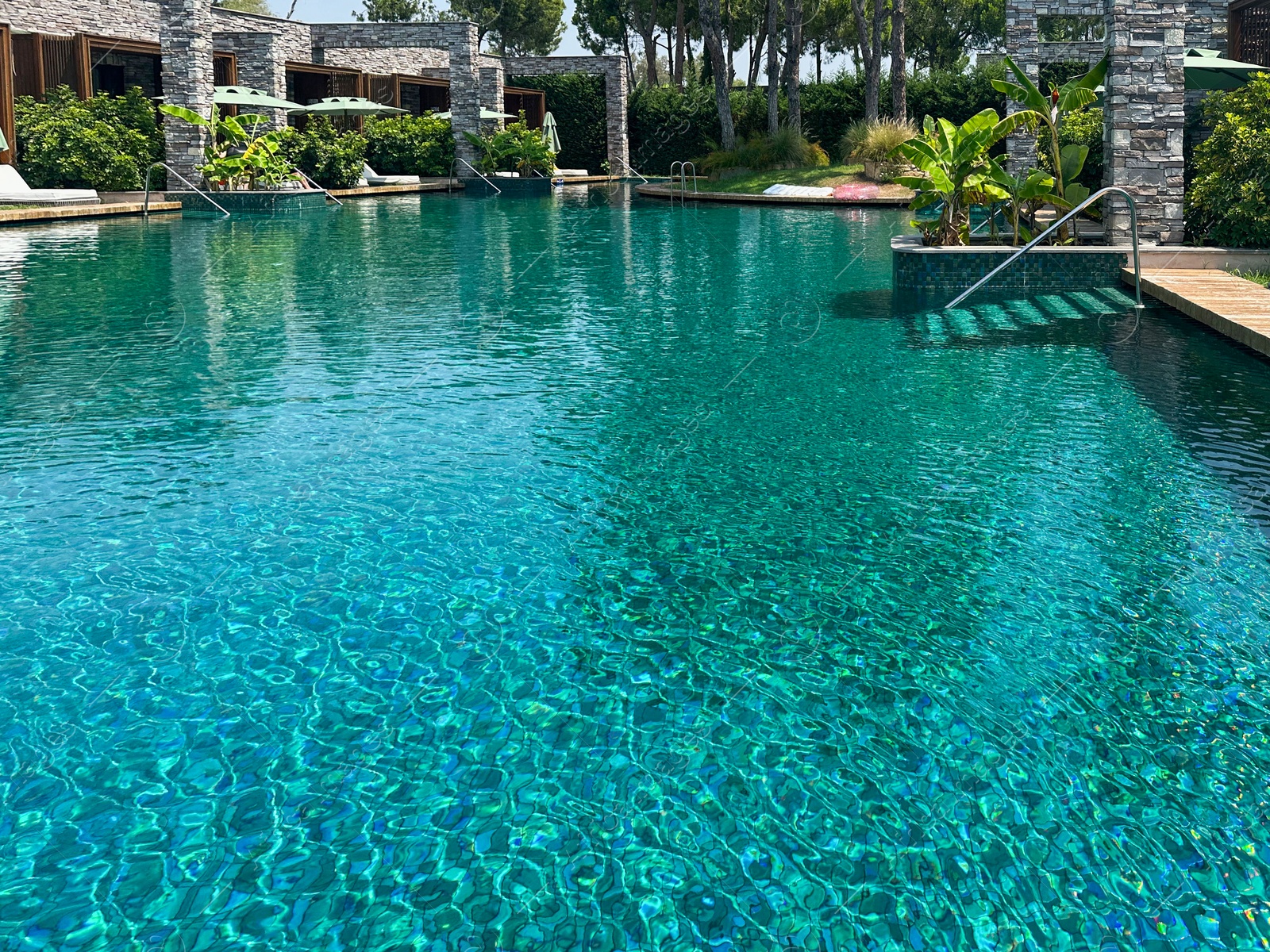 Photo of Outdoor swimming pool with wooden deck on sunny day. Luxury resort