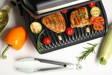 Electric grill with tasty meat, spices and vegetables on white table, flat lay