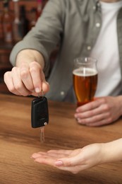 Photo of Man with glass of alcoholic drink giving car key to woman at table, closeup. Don't drink and drive concept