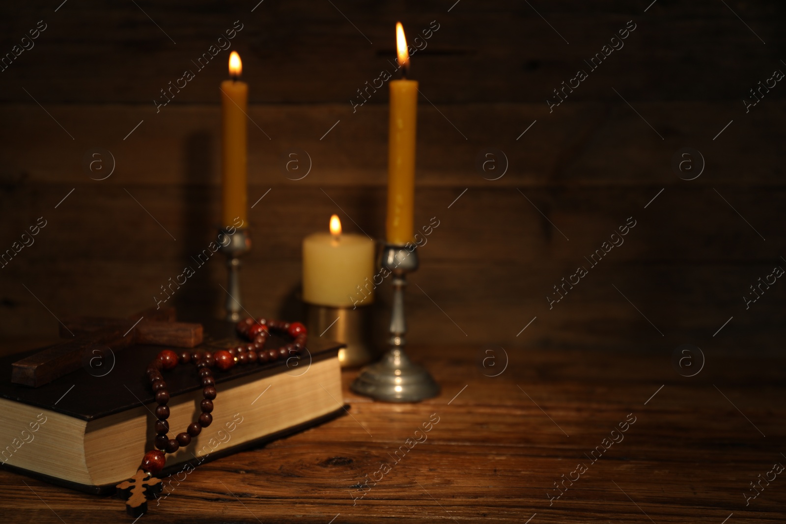 Photo of Church candles, cross, Bible and rosary beads on wooden table, space for text