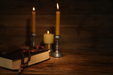 Church candles, cross, Bible and rosary beads on wooden table, space for text