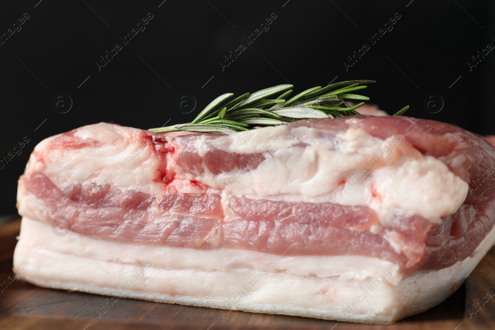 Photo of Piece of raw pork belly, salt and rosemary on wooden board, closeup