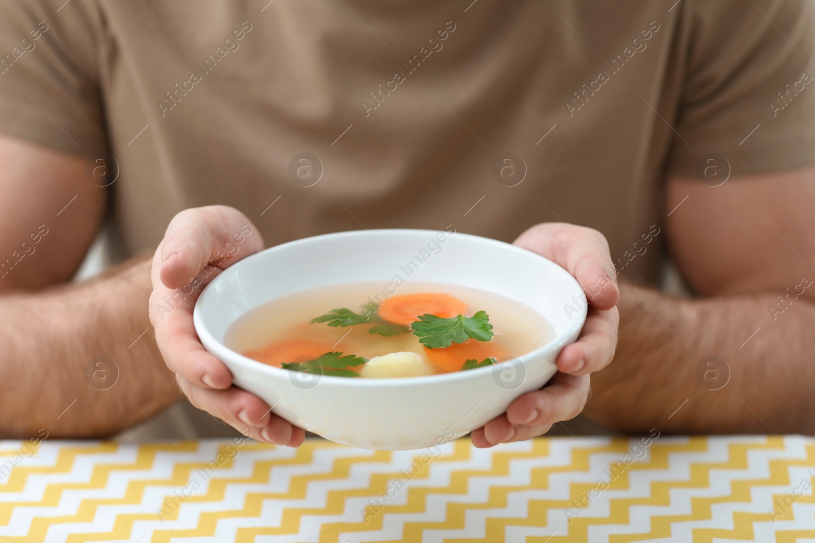 Photo of Young man holding bowl of tasty soup at table, closeup