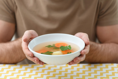 Young man holding bowl of tasty soup at table, closeup