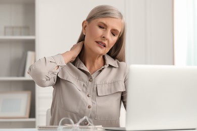 Photo of Woman suffering from neck pain at workplace in room
