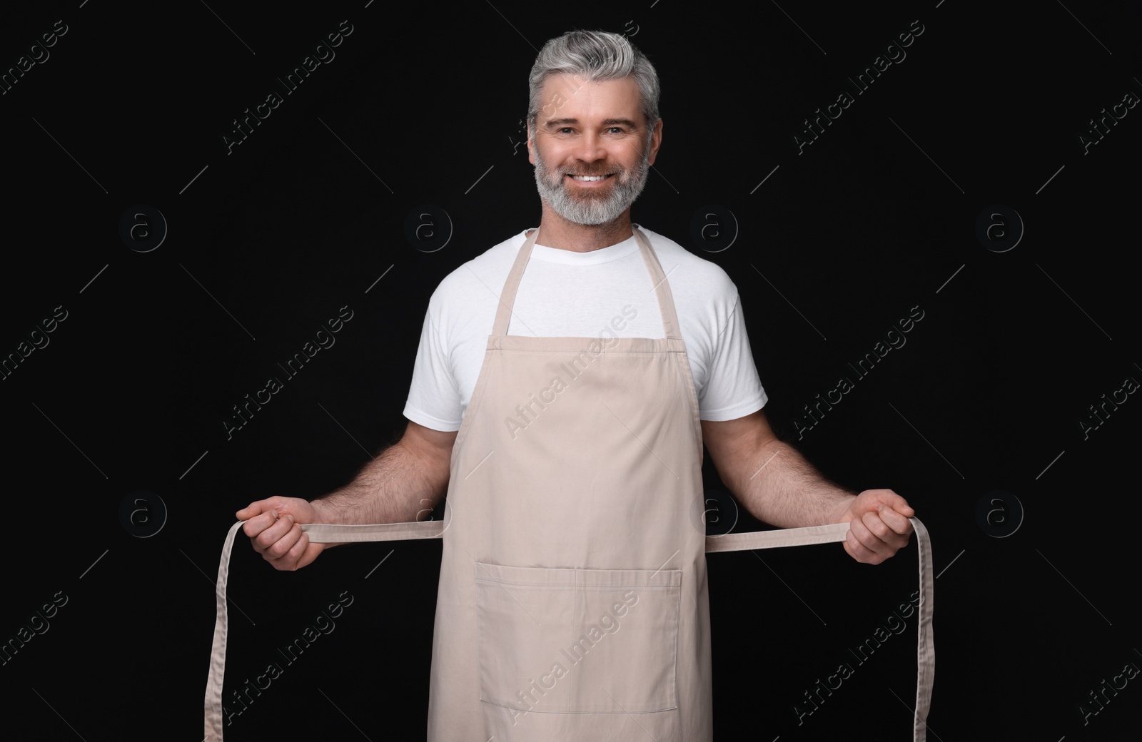 Photo of Happy man wearing kitchen apron on black background. Mockup for design