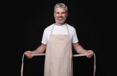 Photo of Happy man wearing kitchen apron on black background. Mockup for design