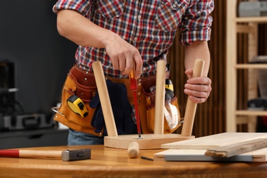 Photo of Young working man repairing wooden stool using screwdriver indoors, closeup