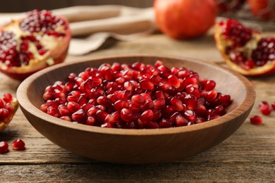 Photo of Ripe juicy pomegranate grains in bowl on wooden table, closeup