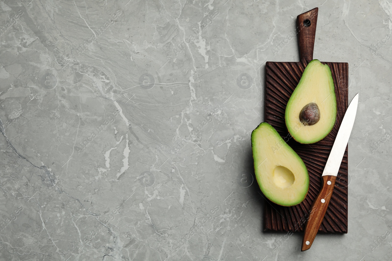 Photo of Halves of delicious ripe avocado on grey marble table, top view. Space for text