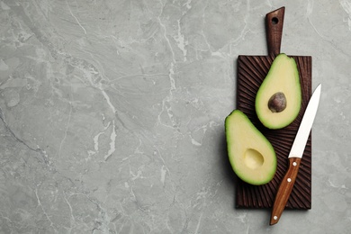 Halves of delicious ripe avocado on grey marble table, top view. Space for text