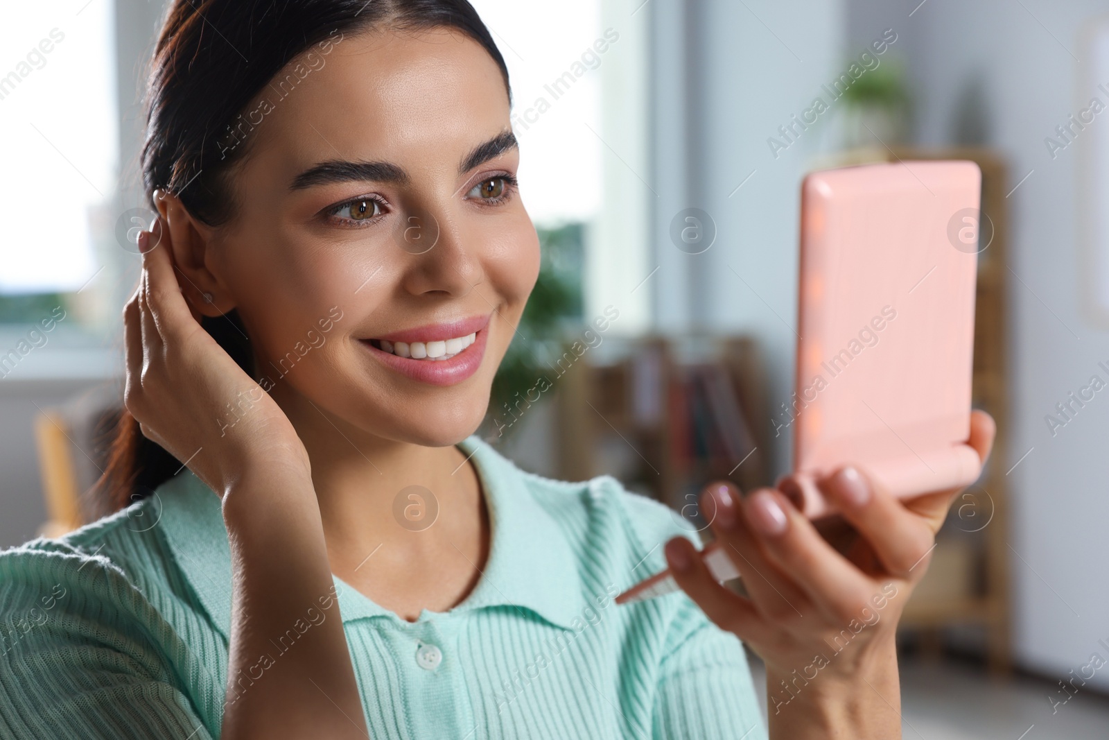 Photo of Young woman looking at cosmetic pocket mirror indoors