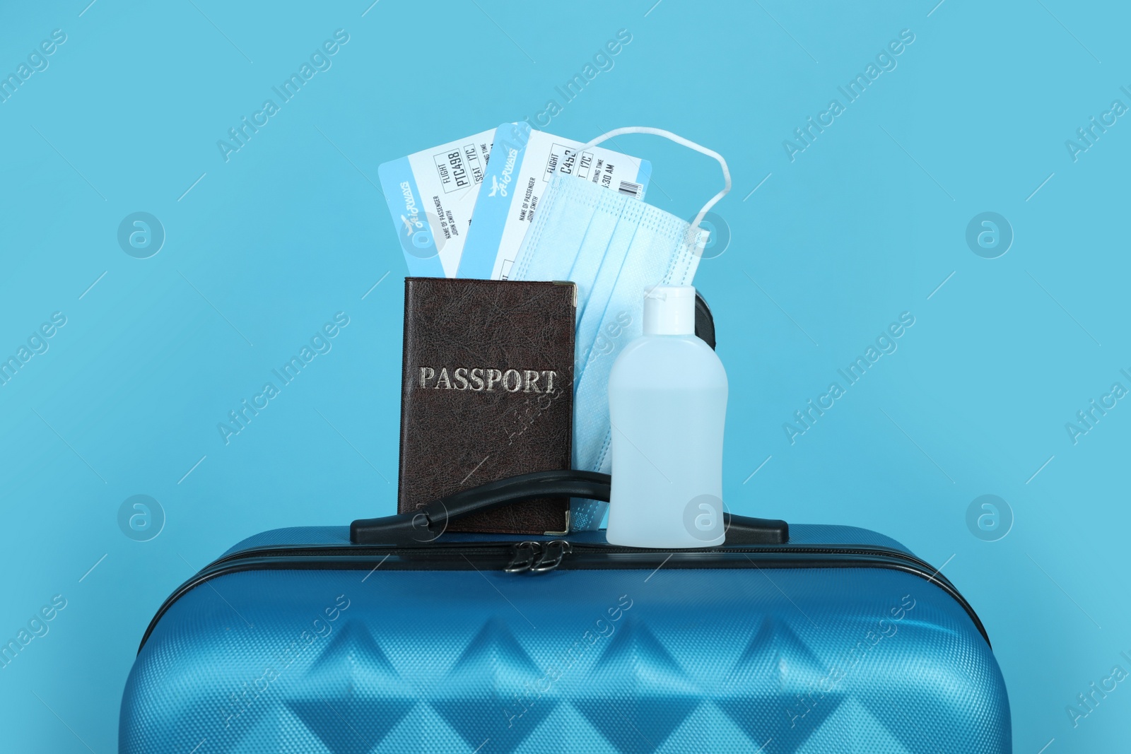 Photo of Passport with tickets, sanitizer and protective mask on suitcase against light blue background. Travel during quarantine