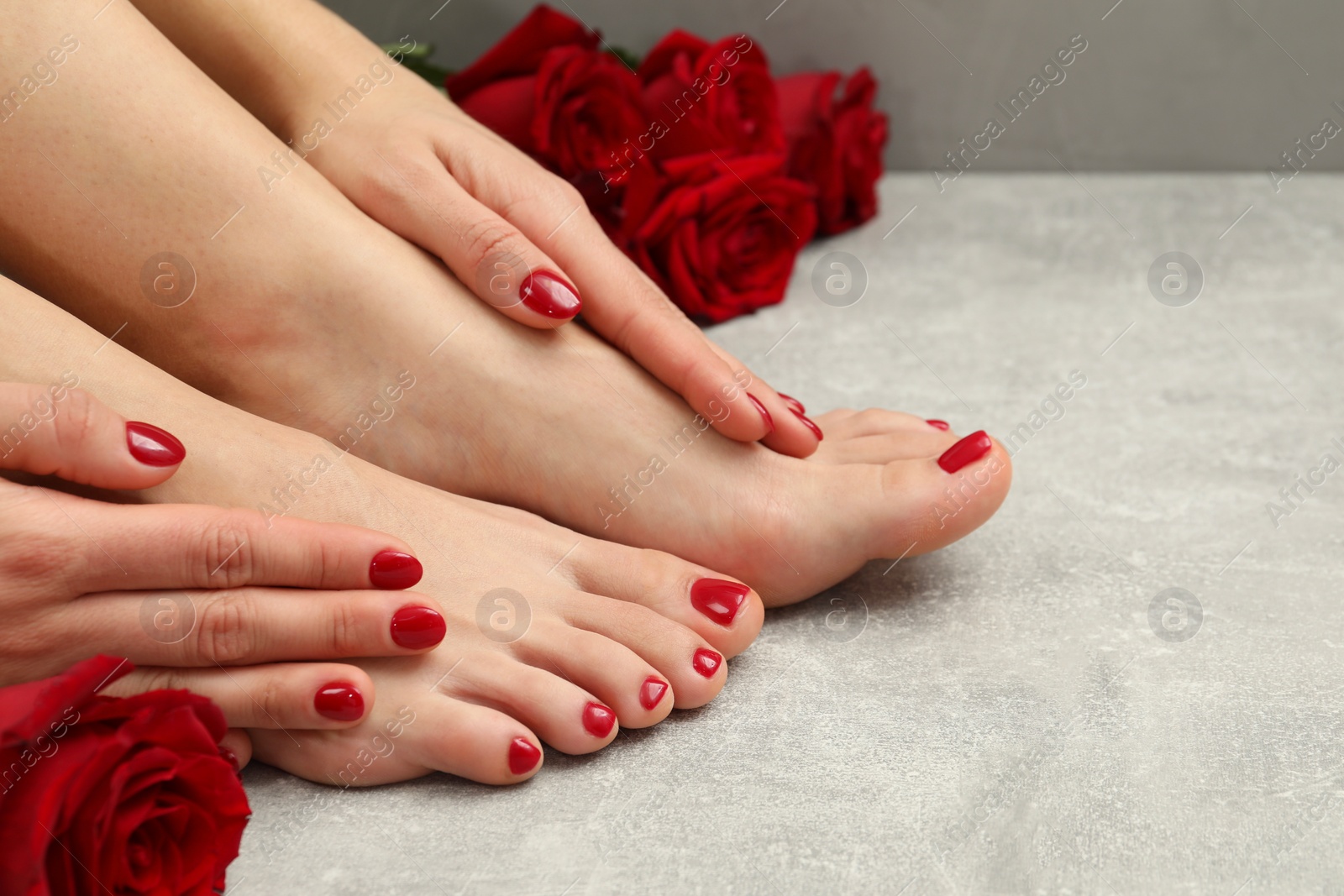 Photo of Woman with stylish red toenails after pedicure procedure and rose flowers on grey textured floor, closeup. Space for text