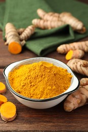 Photo of Bowl with aromatic turmeric powder and cut roots on wooden table