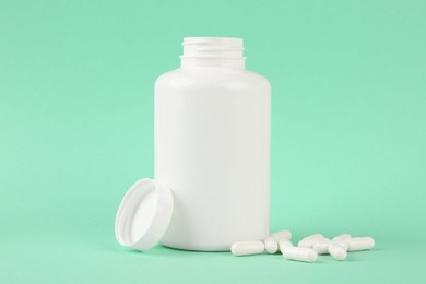 Photo of Blank white jar with vitamin capsules on turquoise background, space for text