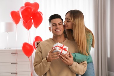 Woman presenting gift to her boyfriend in room decorated with heart shaped balloons. Valentine's day celebration