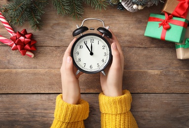 Woman holding alarm clock near Christmas decor over wooden background, top view. New Year countdown
