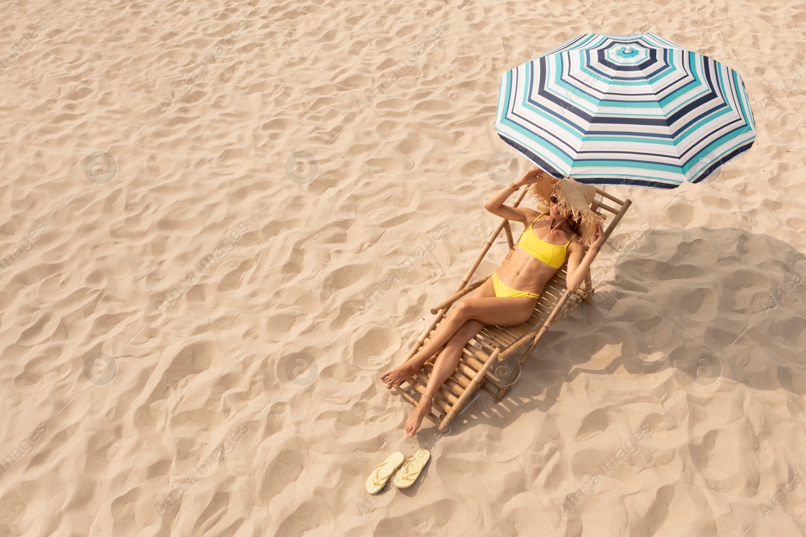 Image of Woman resting in sunbed under striped beach umbrella at sandy coast, space for text