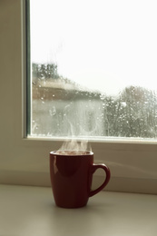 Cup of hot drink near window on rainy day. Space for text